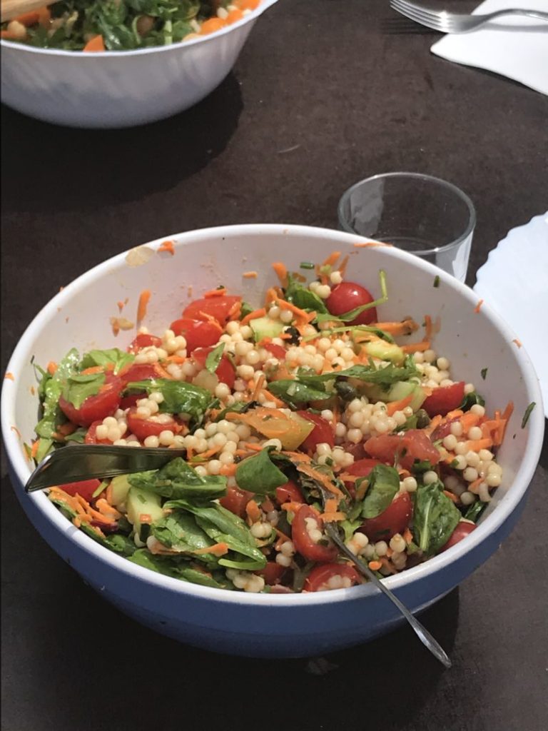 salade d'été de petites pâtes sardes fregola avec des tomates cerise, des carottes râpées, des pousses d'épinard au basilic